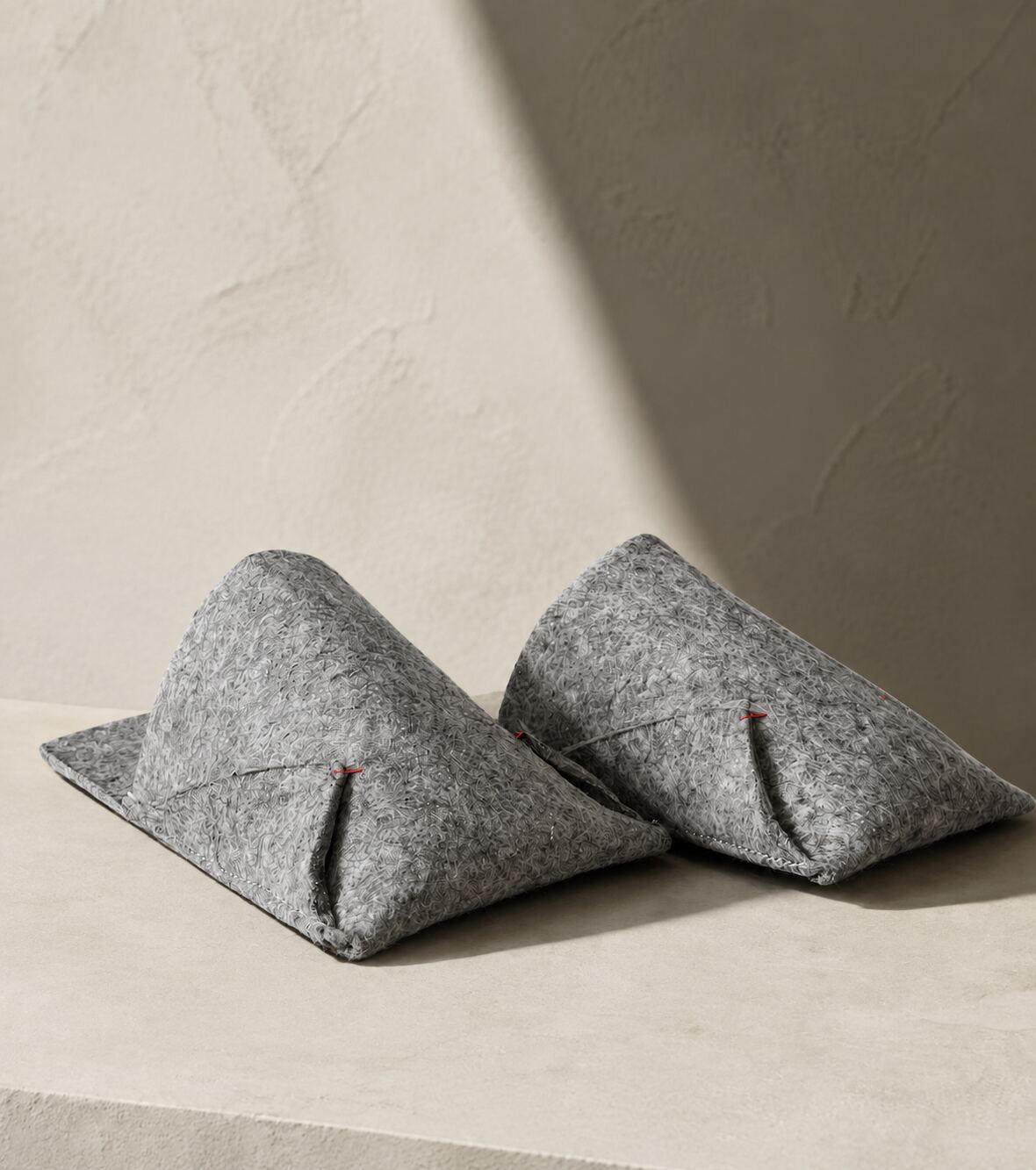 Pair of grey felted wool BAABUK slippers resting on a pale stone bench in soft daylight