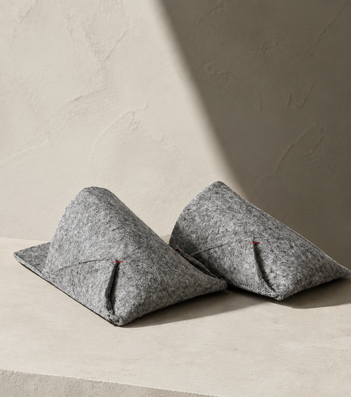 Pair of grey felted wool BAABUK slippers resting on a pale stone bench in soft daylight